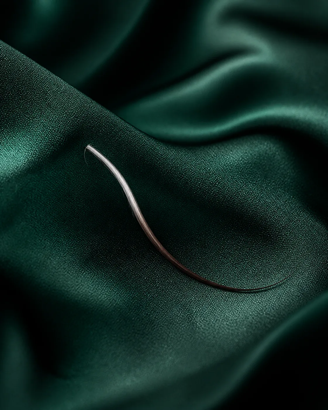 Macro photograph of a dark hair strand with a silver section near the root on emerald silk